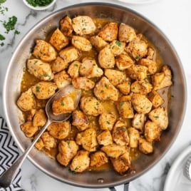 Chicken bites simmering in garlic butter with a spoon in the pan.