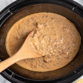overhead of crockpot of rotel dip with a wooden spoon serving some of the dip