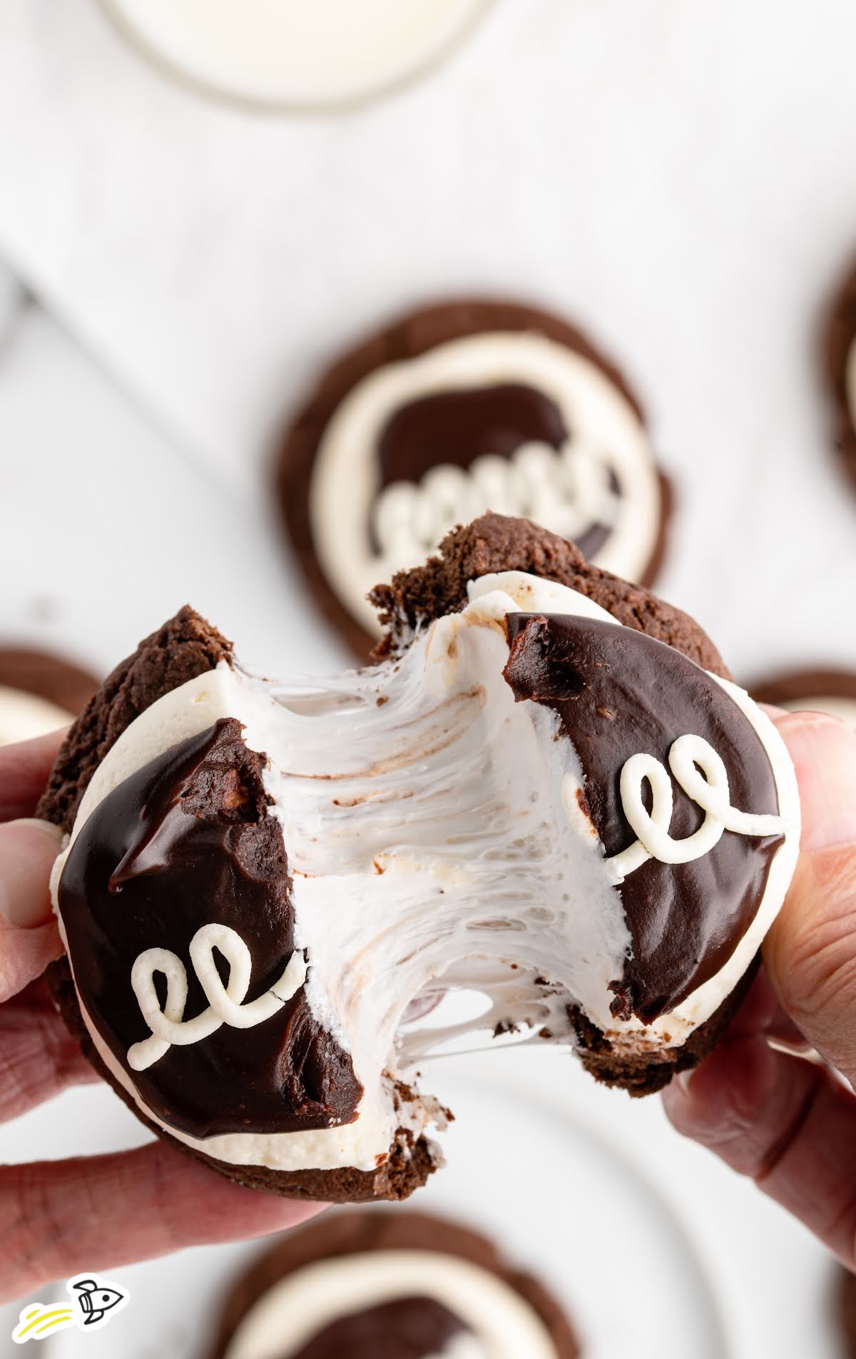 thick, fudgy cookies topped with vanilla frosting and chocolate ganache being pulled apart