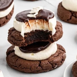 Multiple homemade hostess cupcake cookies on a white surface, featuring rich chocolate cookies topped with cream filling and ganache.