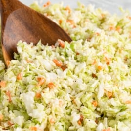 Chopped coleslaw with finely shredded cabbage and carrots, mixed in a bowl, just like the classic KFC Copycat Coleslaw Recipe, with a wooden spoon resting in the mixture.