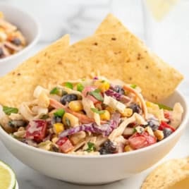 A bowl of taco coleslaw with chicken, black beans, corn, and peppers, served with tortilla chips.