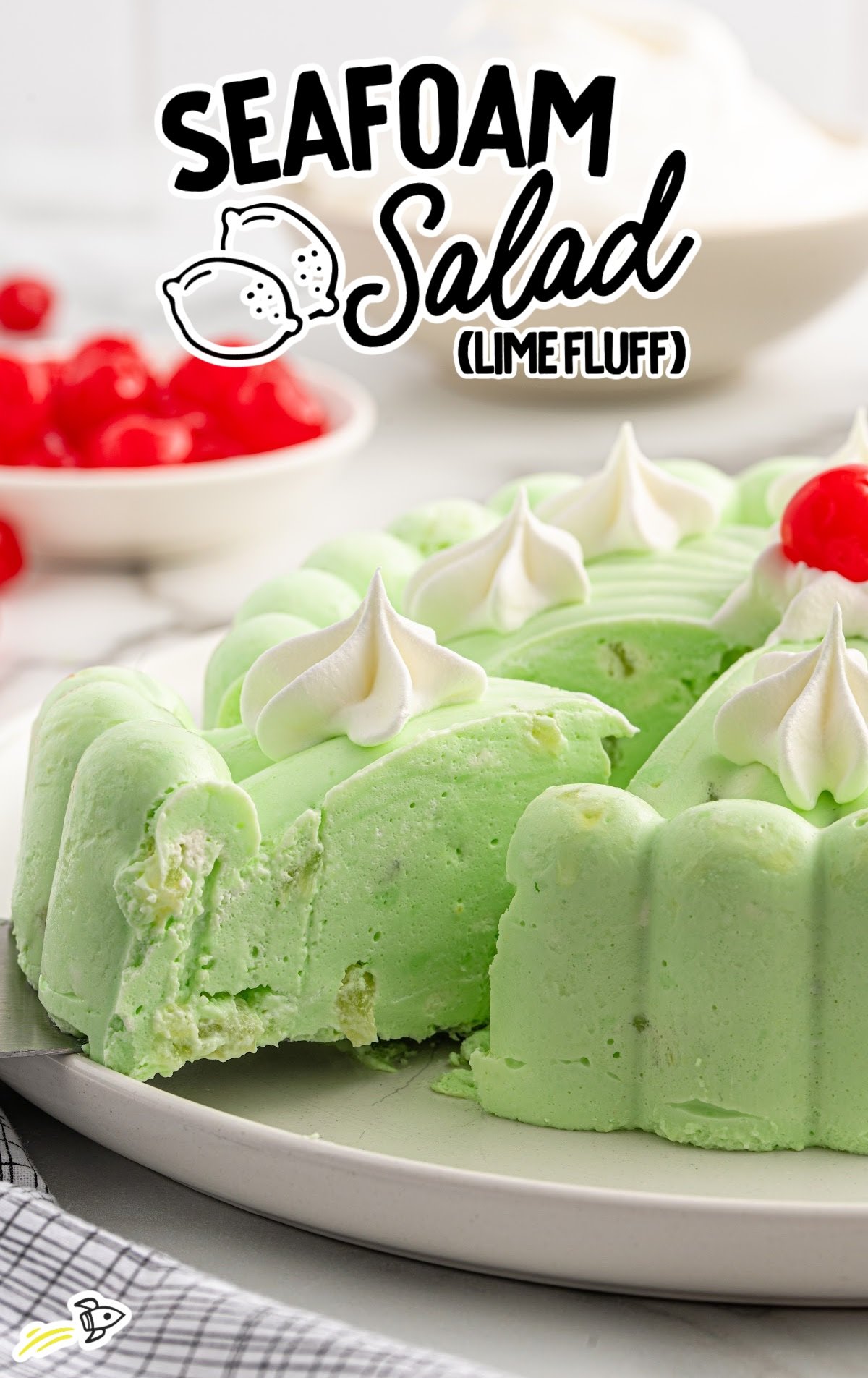 Close-up of seafoam salad with one slice removed, showing creamy lime fluff texture and bits of pear inside, topped with whipped cream and cherries.