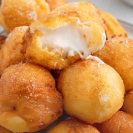 Pile of deep-fried marshmallows with one split open to show melted marshmallow inside.