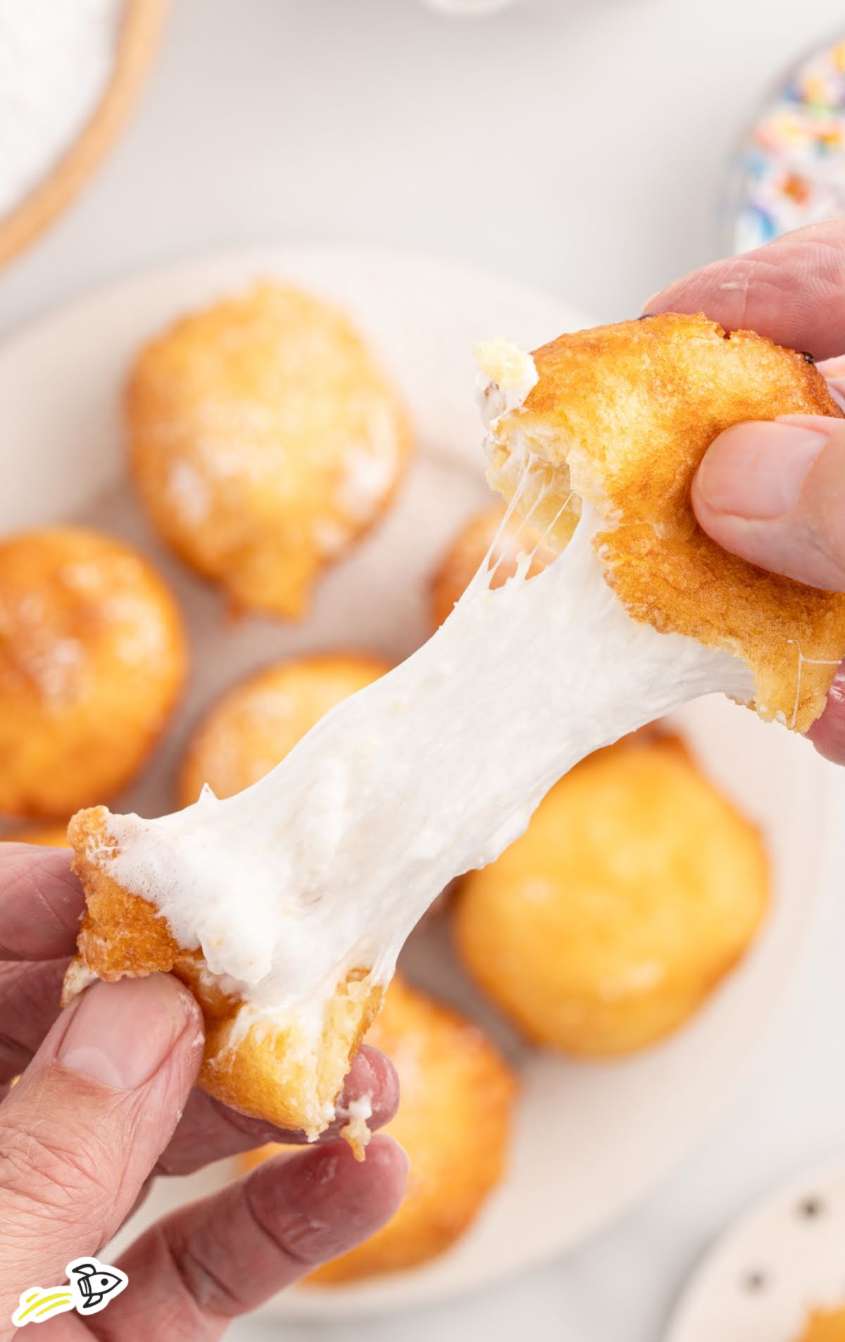 Hands pulling apart a deep-fried marshmallow with a stretchy, gooey marshmallow center.