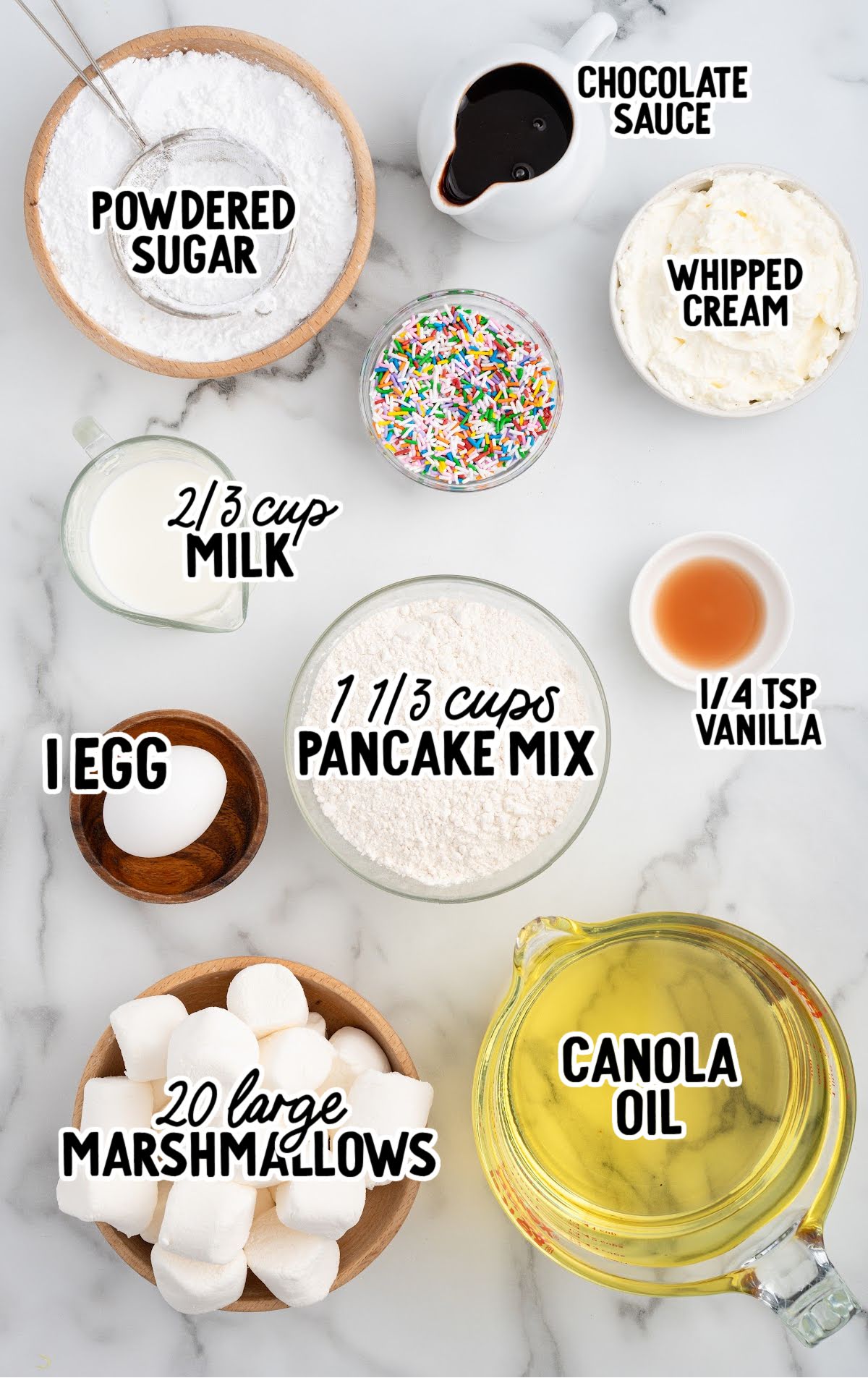 Overhead view of ingredients for deep-fried marshmallows including pancake mix, marshmallows, canola oil, milk, egg, and toppings.
