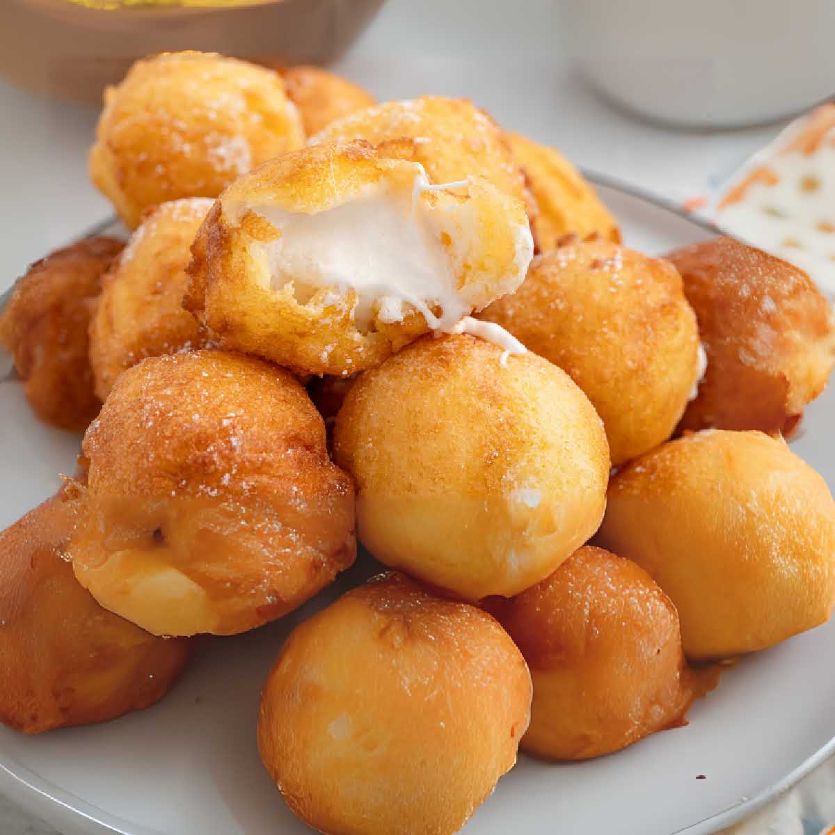 Plate of deep-fried marshmallows with one bitten open, revealing melted inside.
