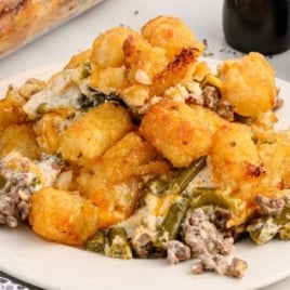 Overhead view of hamburger tater tot casserole in a glass baking dish with a serving spoon and a portion missing.