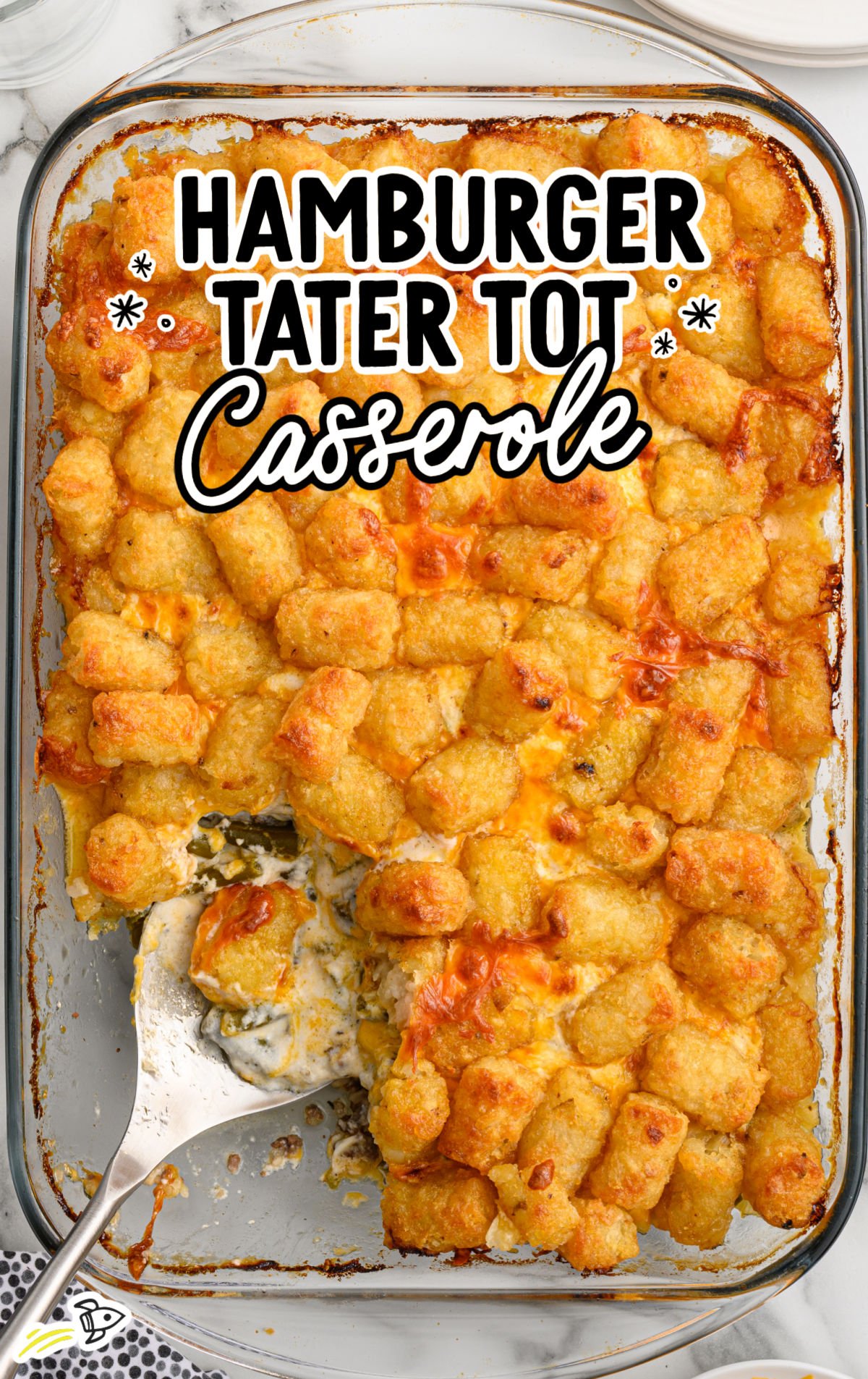 Cheesy tater tot casserole with ground beef and green beans served on a white plate in front of the baking dish.