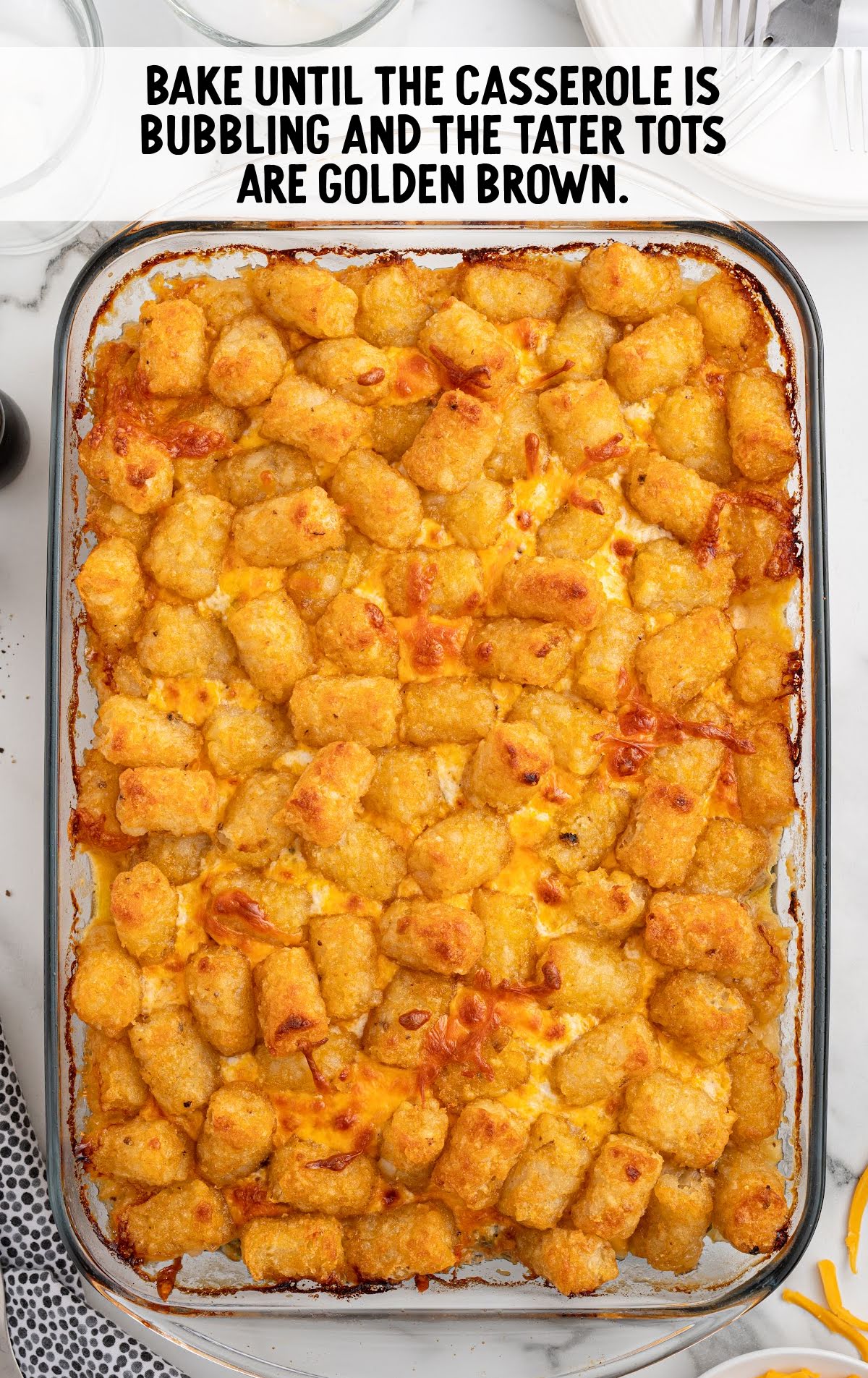 Fully baked casserole with crispy golden tater tots on top and text overlay: “Bake until the casserole is bubbling and the tater tots are golden brown.”