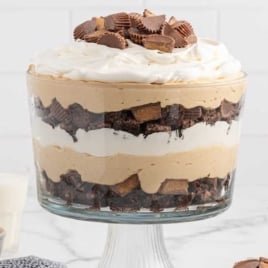 Layered peanut butter trifle in a glass bowl with whipped cream and chopped Reese’s on top.