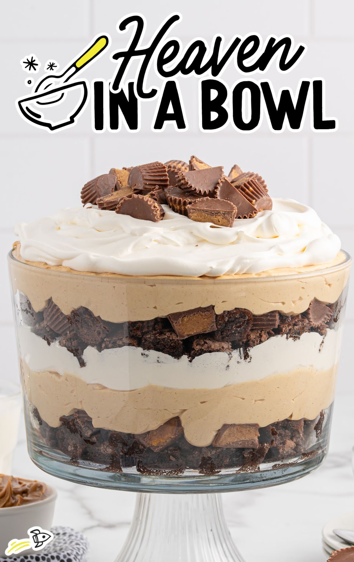 Layered peanut butter trifle in a glass bowl with whipped cream and chopped Reese’s on top.