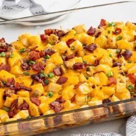 Glass baking dish filled with baked Mississippi Mud Potatoes topped with melted cheddar cheese, bacon, and green onions.