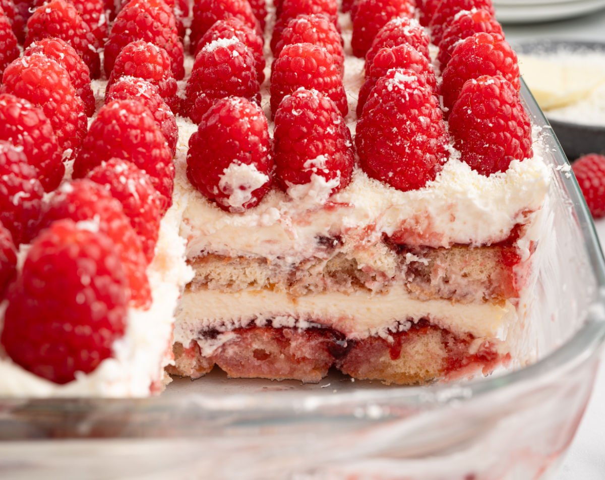 white chocolate raspberry tiramisu on a white plate, topped with fresh raspberries and white chocolate shavings.
