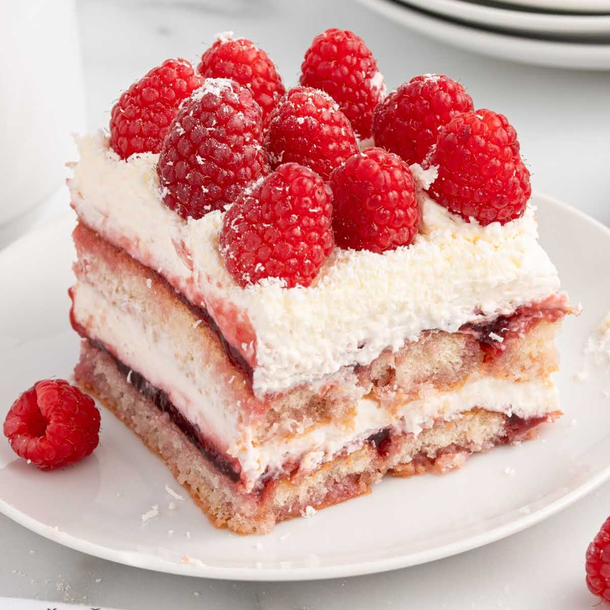 Single serving of white chocolate raspberry tiramisu with layers of soaked ladyfingers, whipped cream, and raspberries on a white plate.