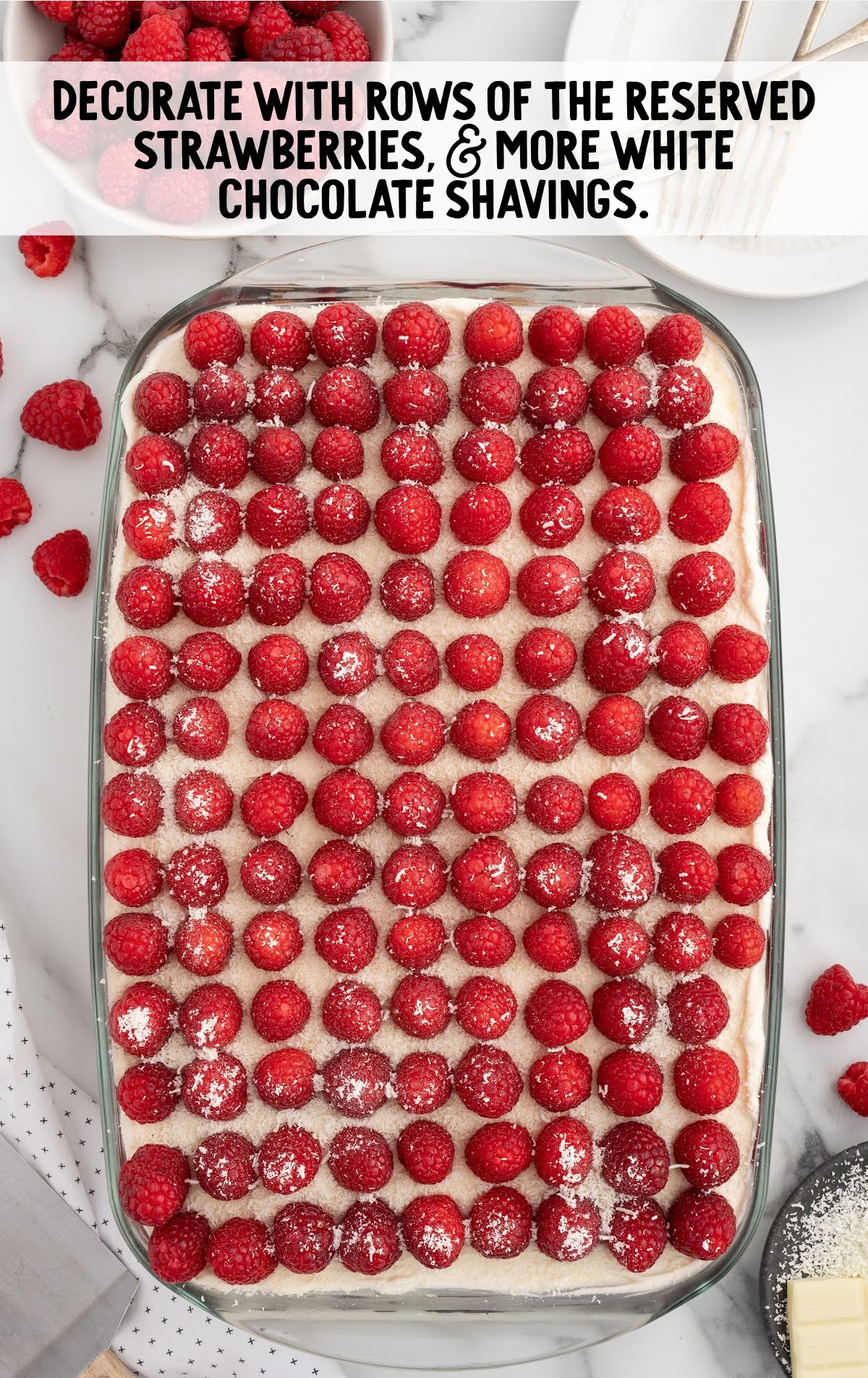 Finished white chocolate raspberry tiramisu topped with neat rows of fresh raspberries and dusted with white chocolate shavings.