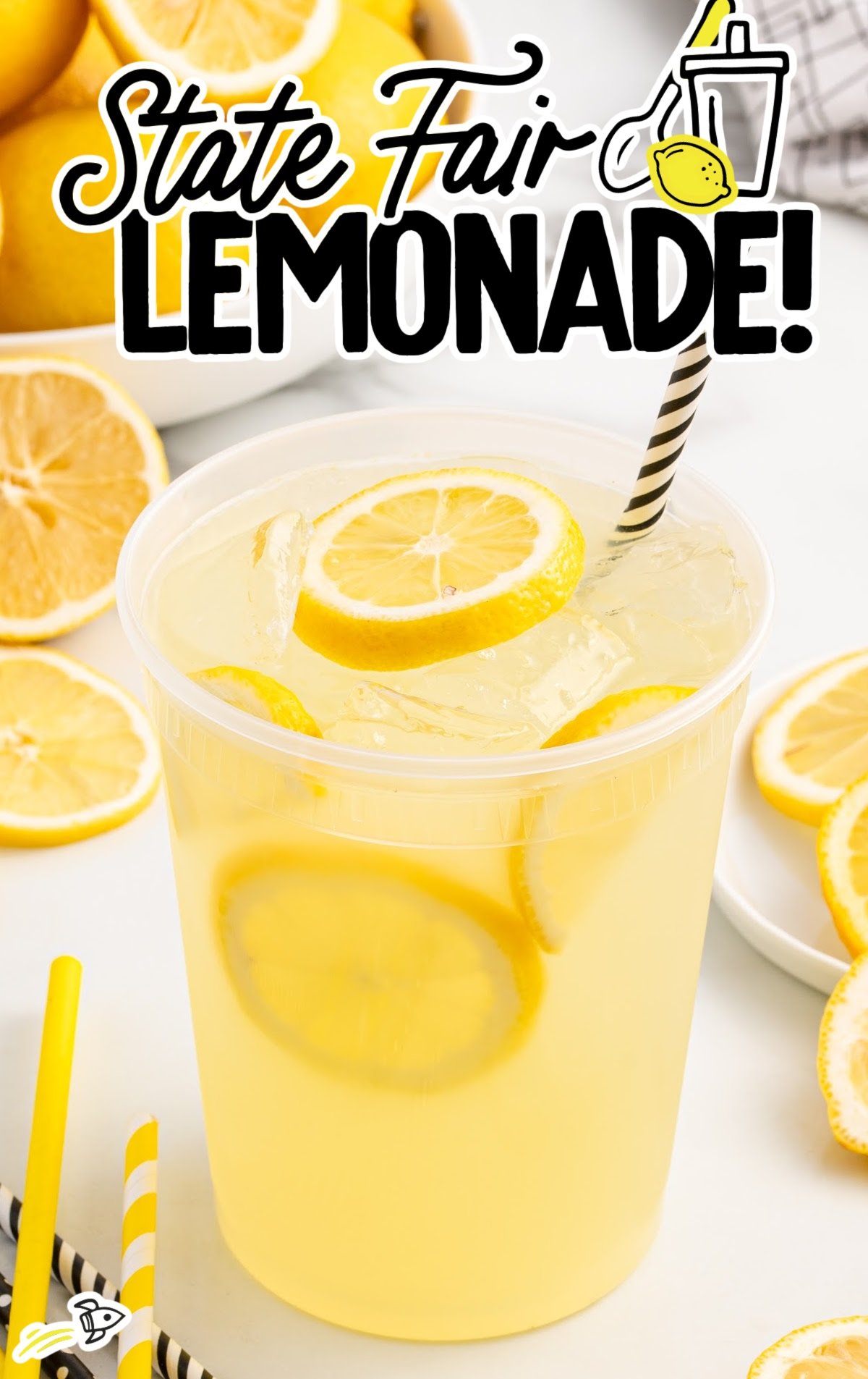 Plastic cup of state fair lemonade with lemon slices and black striped straw surrounded by lemon slices and straws.