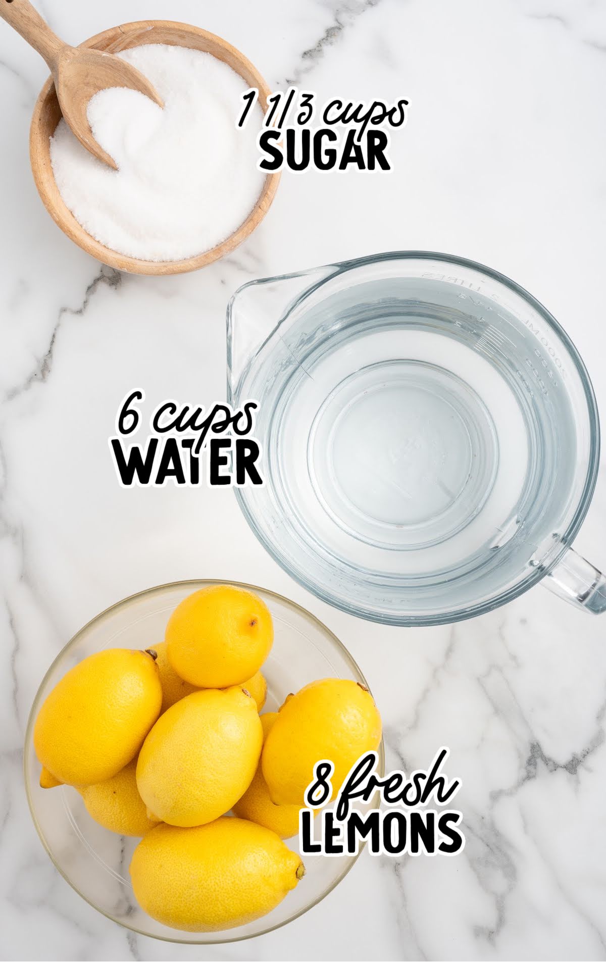Ingredients for state fair lemonade including a bowl of sugar, a pitcher of water, and fresh lemons on a marble counter.