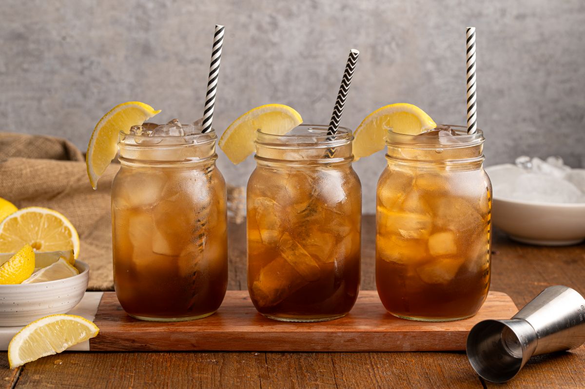 Three mason jars filled with iced tea and lemon wedges, each with a striped straw, sit on a wooden board&mdash;just like a classic Texas Tea Recipe served on a warm afternoon.