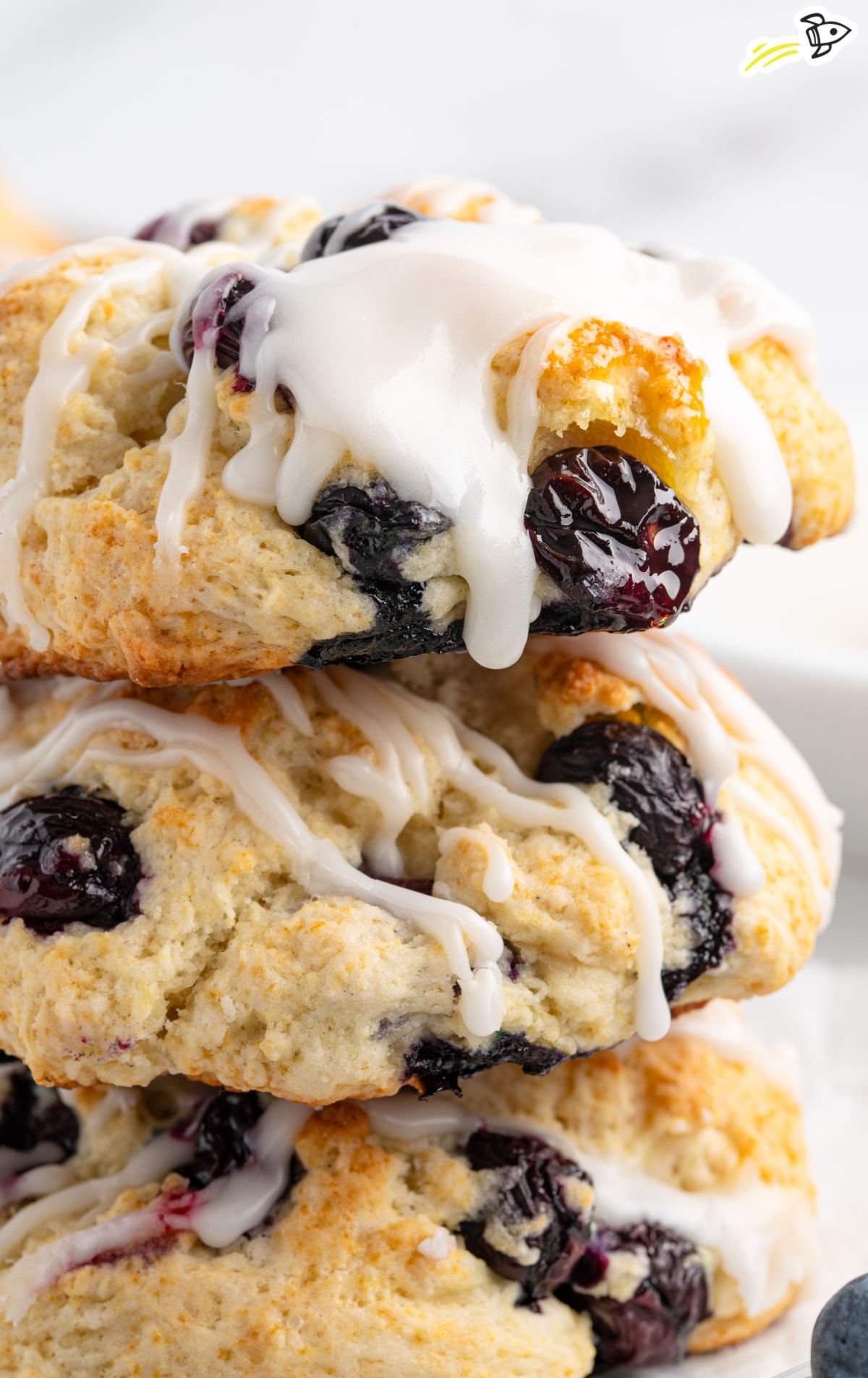 Stack of glazed blueberry biscuits with visible whole berries and a thick drizzle of white icing on top.