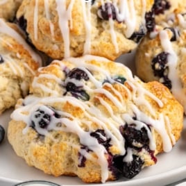 Plate of glazed blueberry biscuits with text overlay: “Old Fashioned Tricks for Perfect Blueberry Biscuits – Apply These Techniques to All Your Biscuits!”