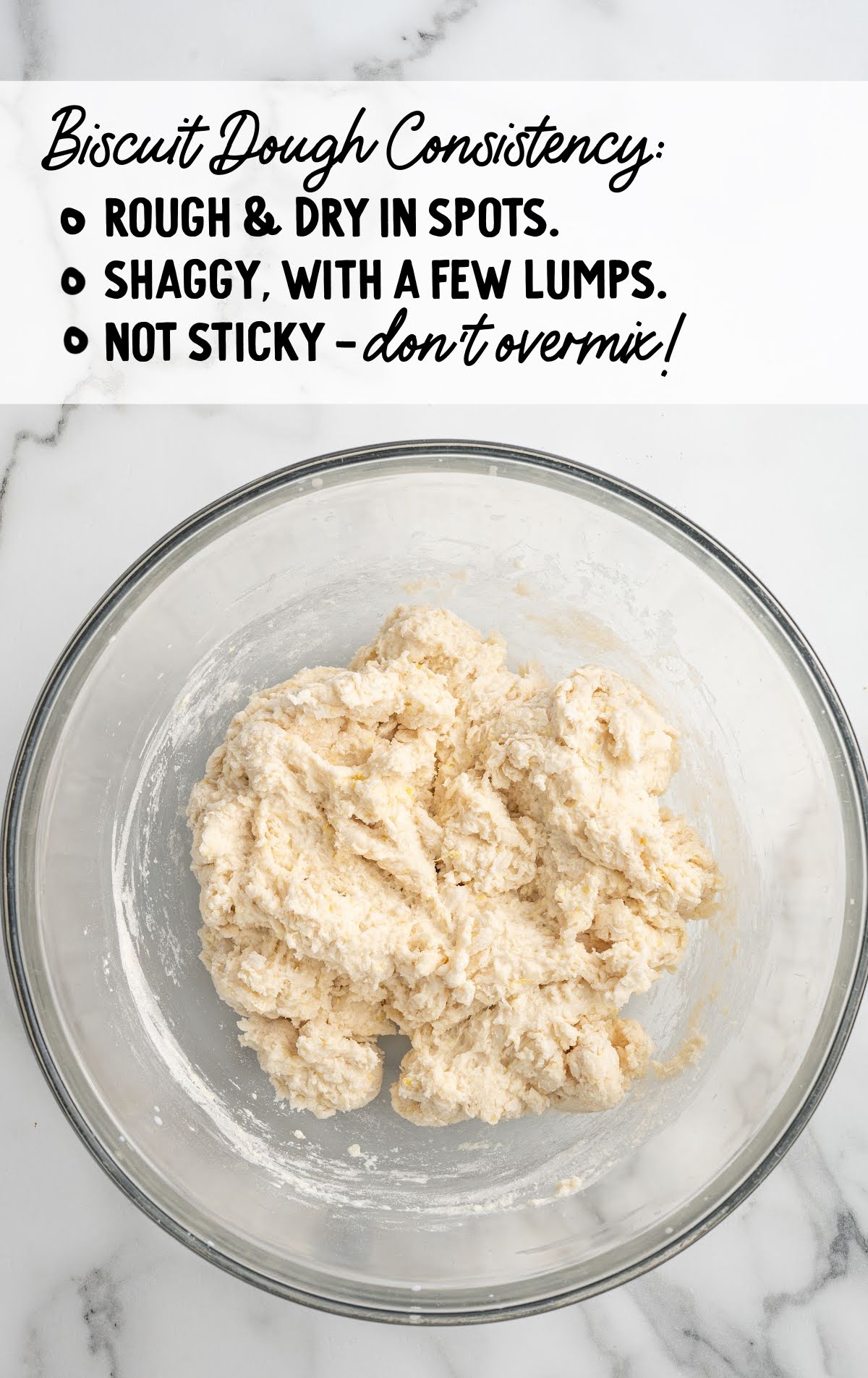 Glass bowl of biscuit dough showing rough, shaggy texture with a note emphasizing not to overmix for best biscuit consistency.