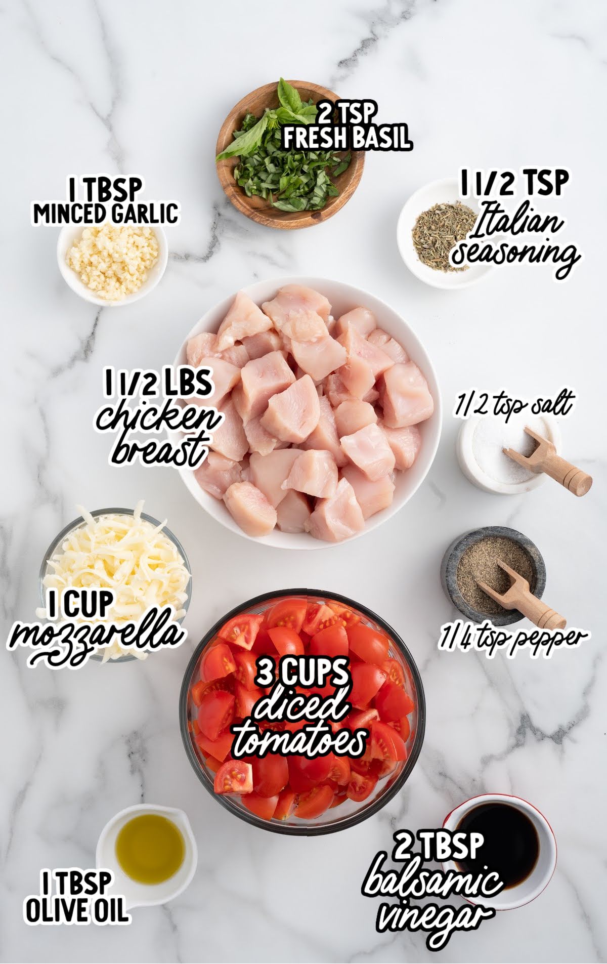 Top-down view of baked bruschetta chicken in a glass dish, garnished with chopped basil, next to a bowl of fresh herbs and stack of white plates.