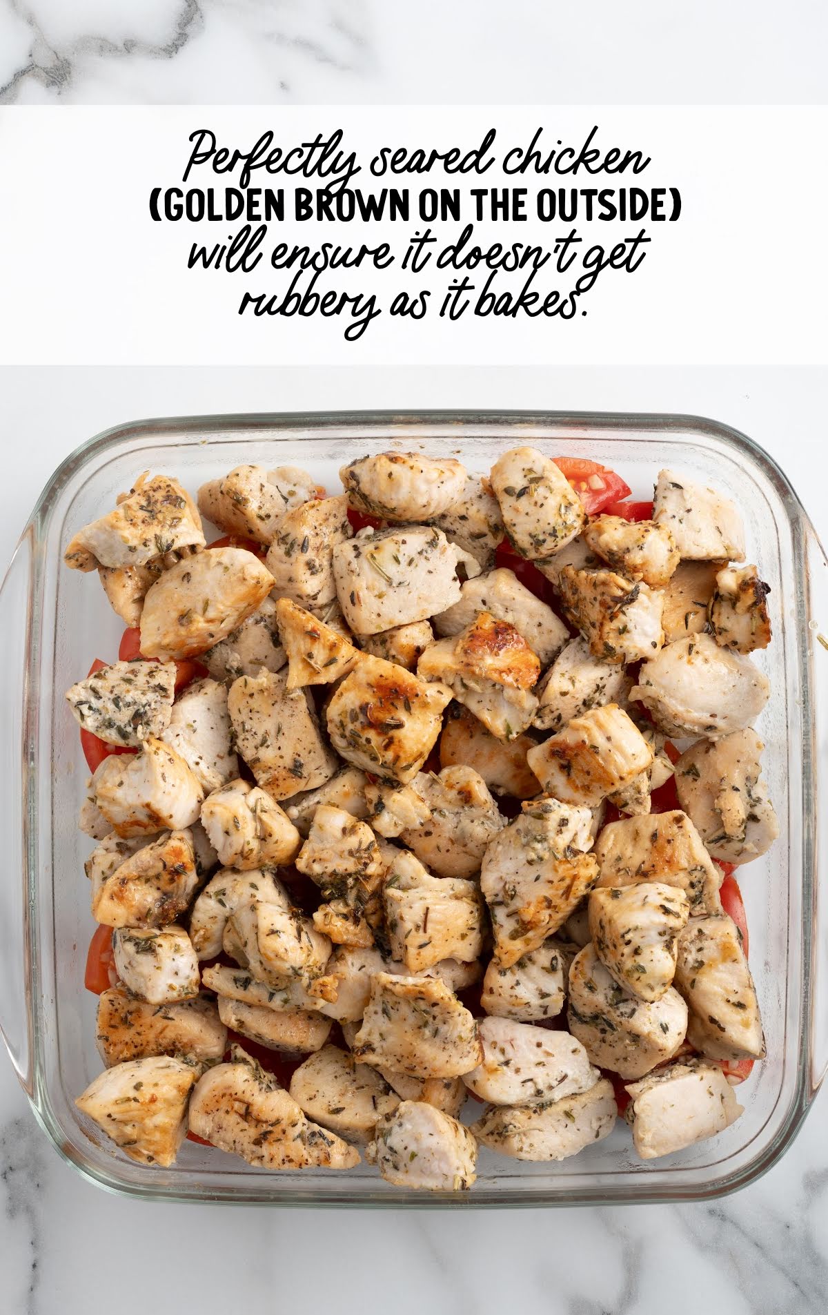 Golden brown seared chicken pieces layered over diced tomatoes in a glass baking dish, ready for baking, with a tip about preventing rubbery chicken.