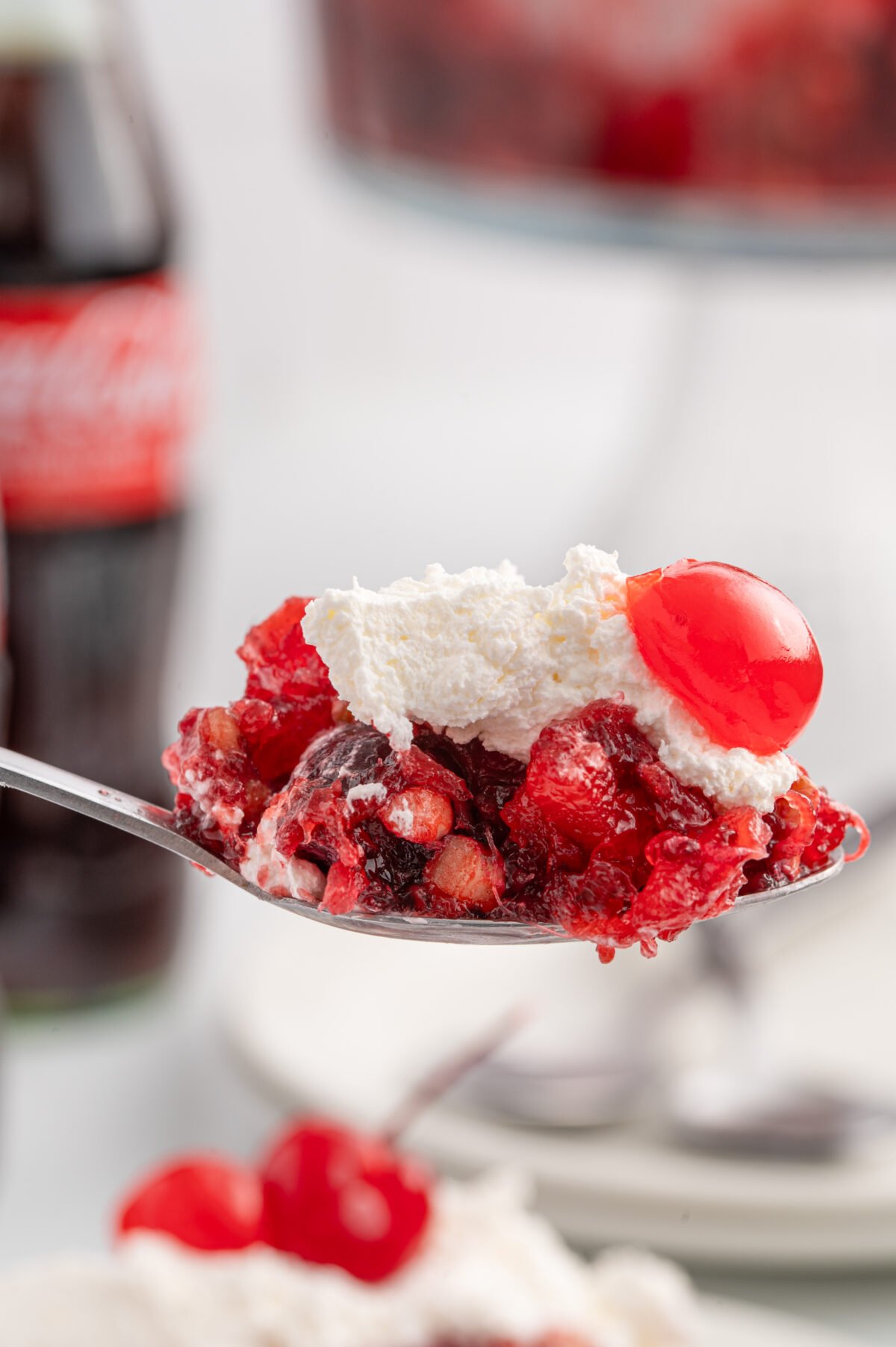 a spoonful of Coca Cola fruit trifle topped with whipped cream and cherries.