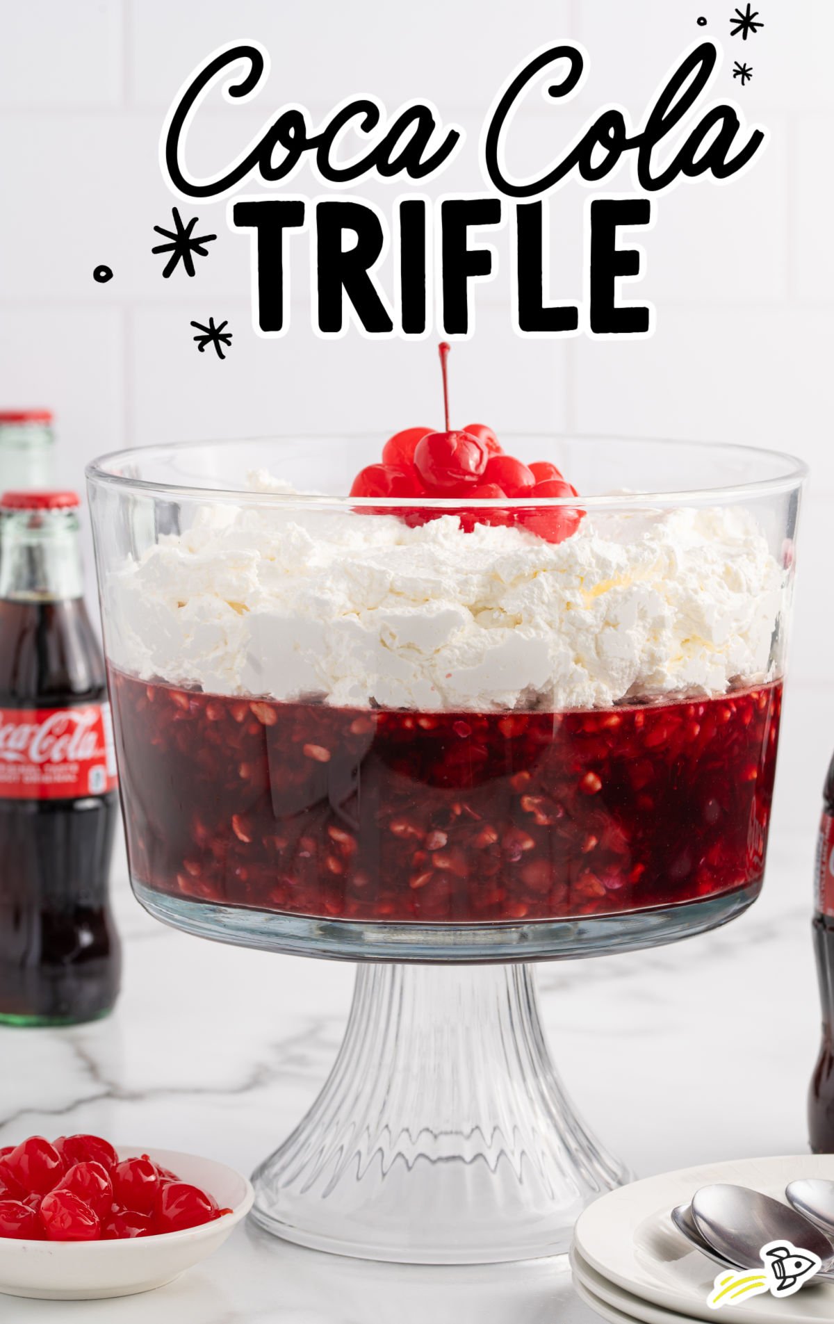 Glass trifle bowl filled with Coca Cola fruit trifle topped with whipped cream and cherries.