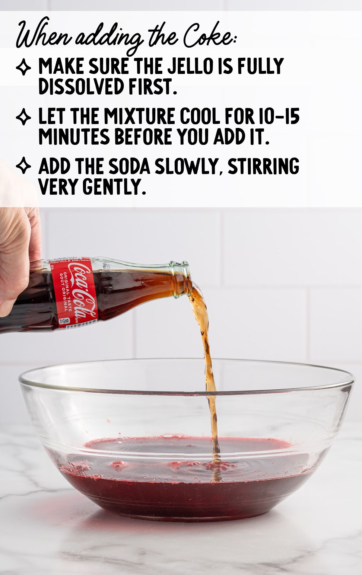Hand pouring Coca-Cola from a glass bottle into a bowl of red liquid (Jello mixture) on a marble countertop. Above the image, there are preparation tips in bold black text: make sure the Jello is fully dissolved, let the mixture cool for 10–15 minutes before adding soda, and pour Coke in slowly while stirring gently.