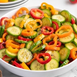 White bowl of cucumber and bell pepper salad on a table
