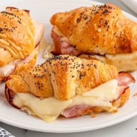 Close-up of baked ham and cheese croissants on a white plate, filled with melted cheese and slices of ham