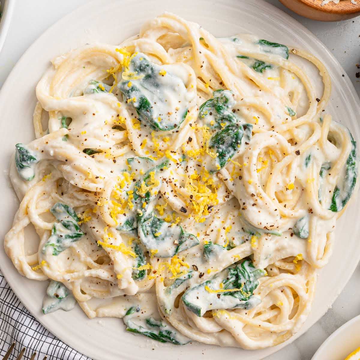 Top-down view of a plate of lemon ricotta pasta with spinach, topped with lemon zest and black pepper.