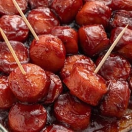 A glass baking dish filled with oven-baked BBQ sausage bites, with a few pieces pierced by toothpicks for serving.