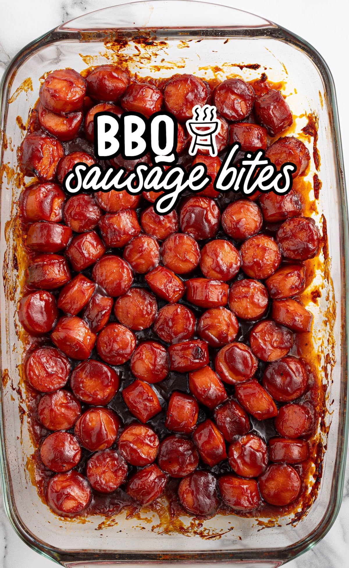 Glass baking dish filled with evenly sliced sausage bites coated in sticky barbecue sauce. Text overlay reads “BBQ Sausage Bites.”