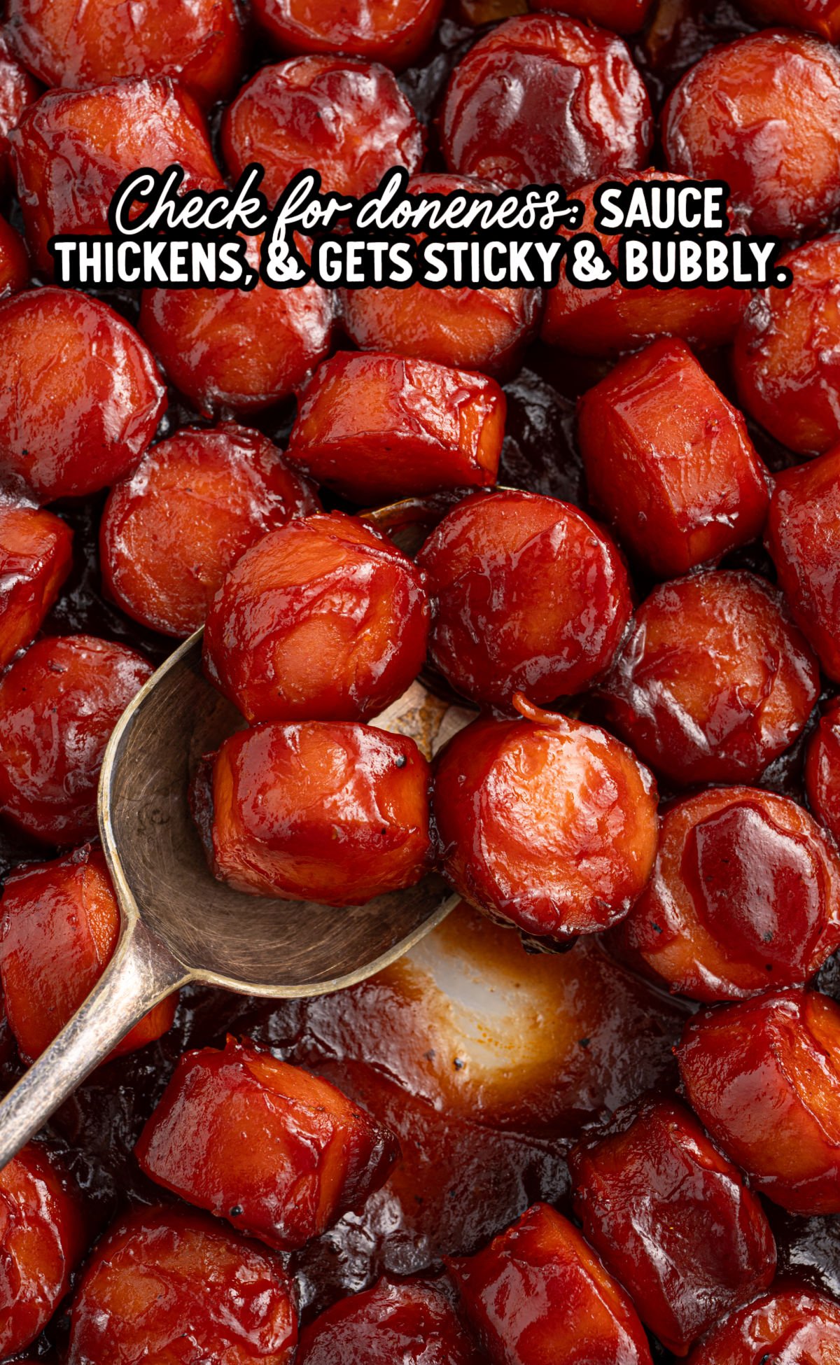 Close-up of sticky BBQ sausage bites with a metal spoon scooping one piece. Text overlay says to check for doneness when sauce thickens and bubbles.