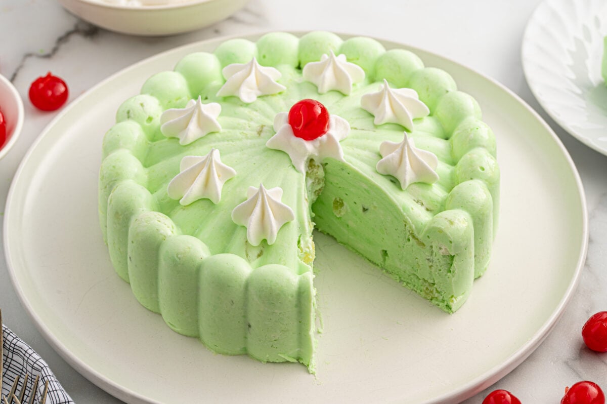 Side angle of a molded green seafoam salad topped with whipped cream dollops and a cherry.