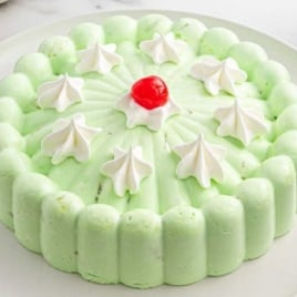 Overhead view of a lime green seafoam salad topped with dollops of whipped cream and a cherry centerpiece.