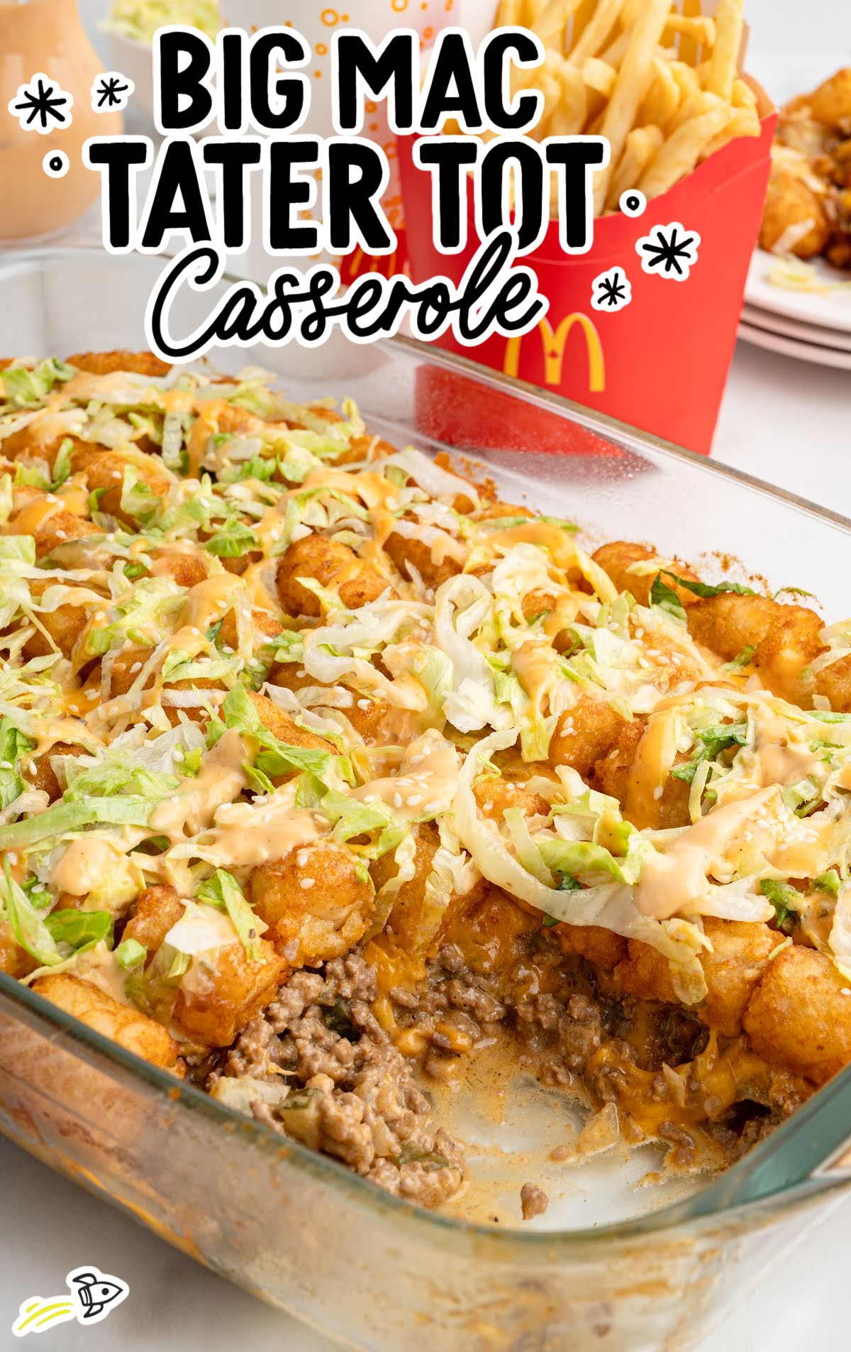 Glass baking dish filled with Big Mac tater tot casserole topped with shredded lettuce, sesame seeds, and drizzle of Thousand Island dressing.