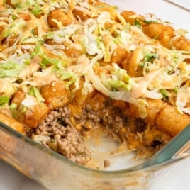 Overhead view of Big Mac tater tot casserole in a glass dish topped with shredded lettuce and sauce drizzle.