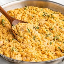 Skillet filled with creamy cheesy chicken orzo with spinach and a wooden spoon