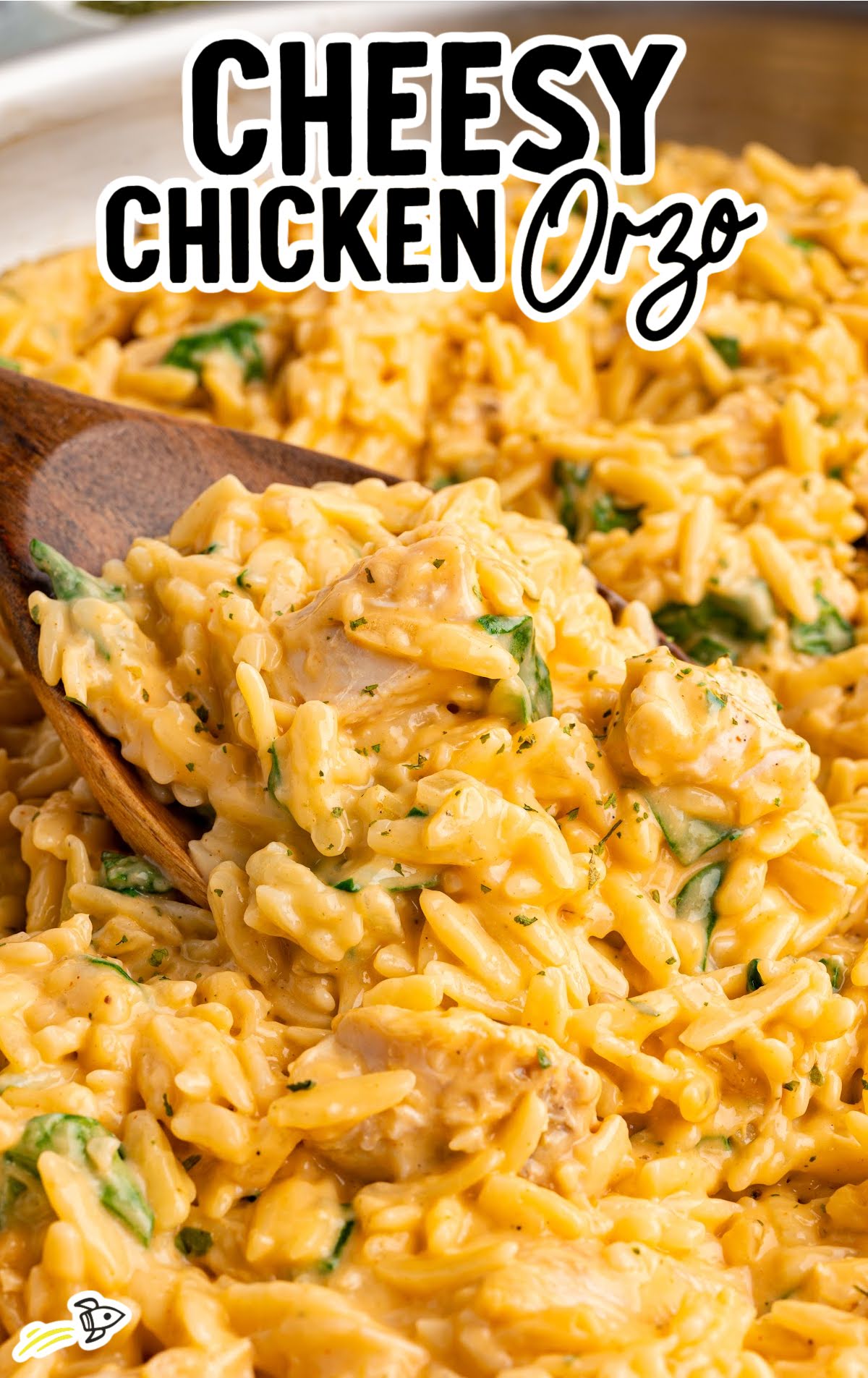 Cheesy chicken orzo being scooped from skillet with text overlay “Cheesy Chicken Orzo”