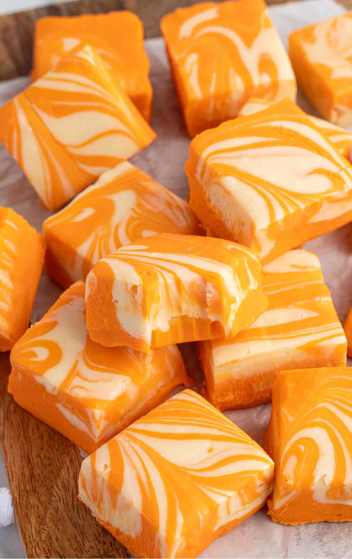 Orange and white swirled creamsicle fudge squares arranged on parchment lined board