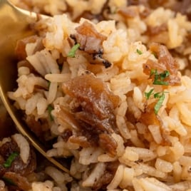 French onion baked rice with caramelized onions and parsley served with a gold spoon.