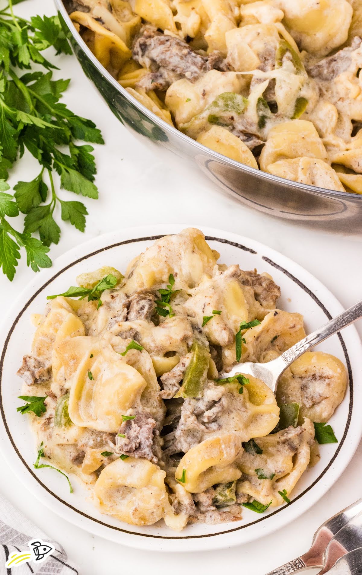 Creamy Philly cheesesteak tortellini on a plate garnished with parsley beside the skillet