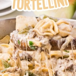 Cheesy Philly cheesesteak tortellini being lifted from the skillet showing melted cheese strings and tender beef