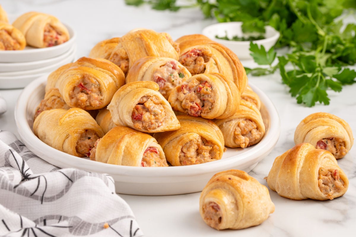Plate of flaky crescent rolls stuffed with sausage, Rotel tomatoes, and cream cheese served on a marble countertop with parsley garnish.