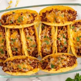 Close-up of golden crispy baked tacos stacked and filled with seasoned beef, melted cheese, and fresh cilantro.
