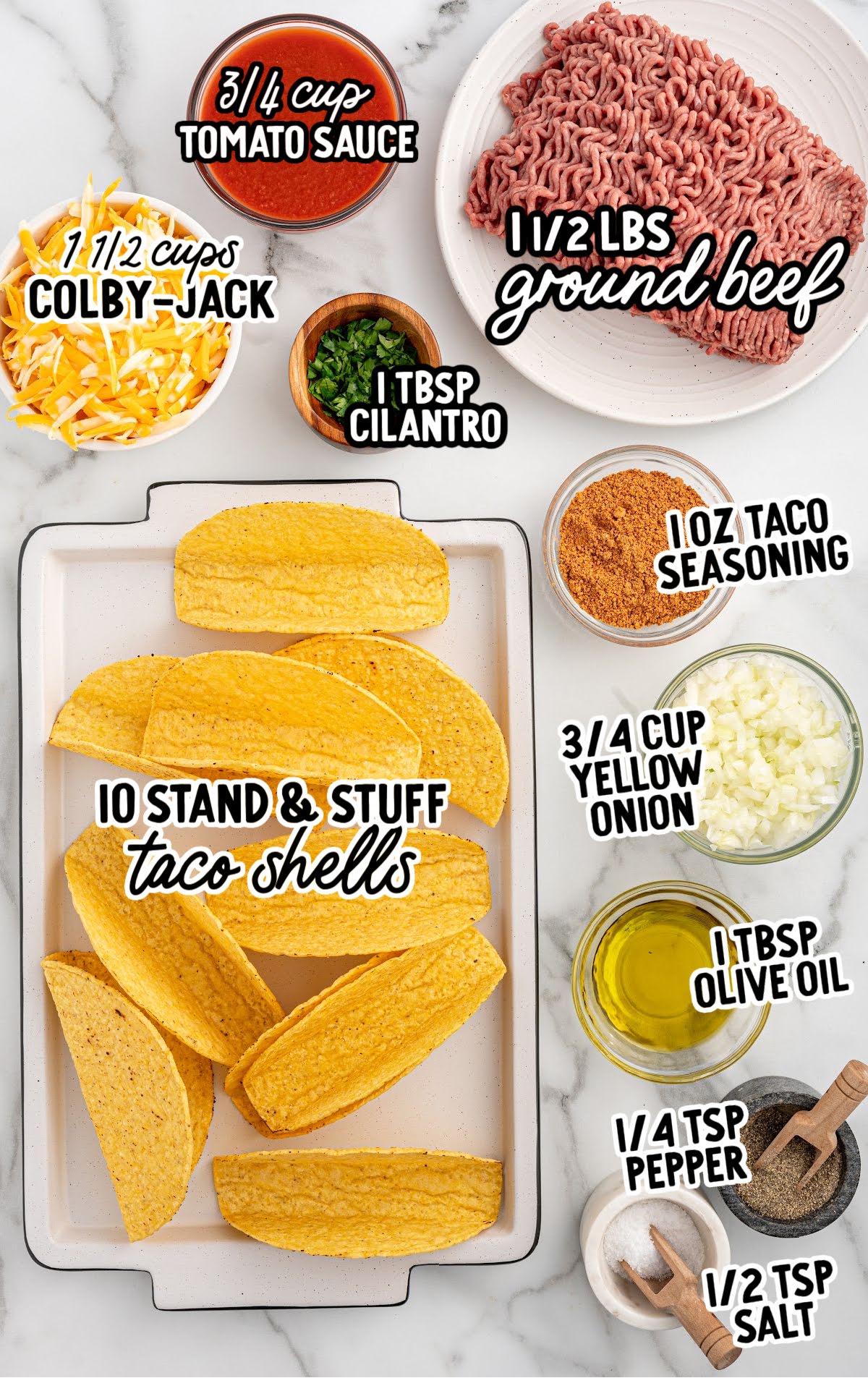 Ingredients for baked tacos including ground beef, taco seasoning, tomato sauce, taco shells, cheese, and cilantro laid out on a marble counter.